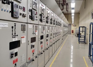 Long row of control panels in an industrial electrical control room, well-lit and spacious.